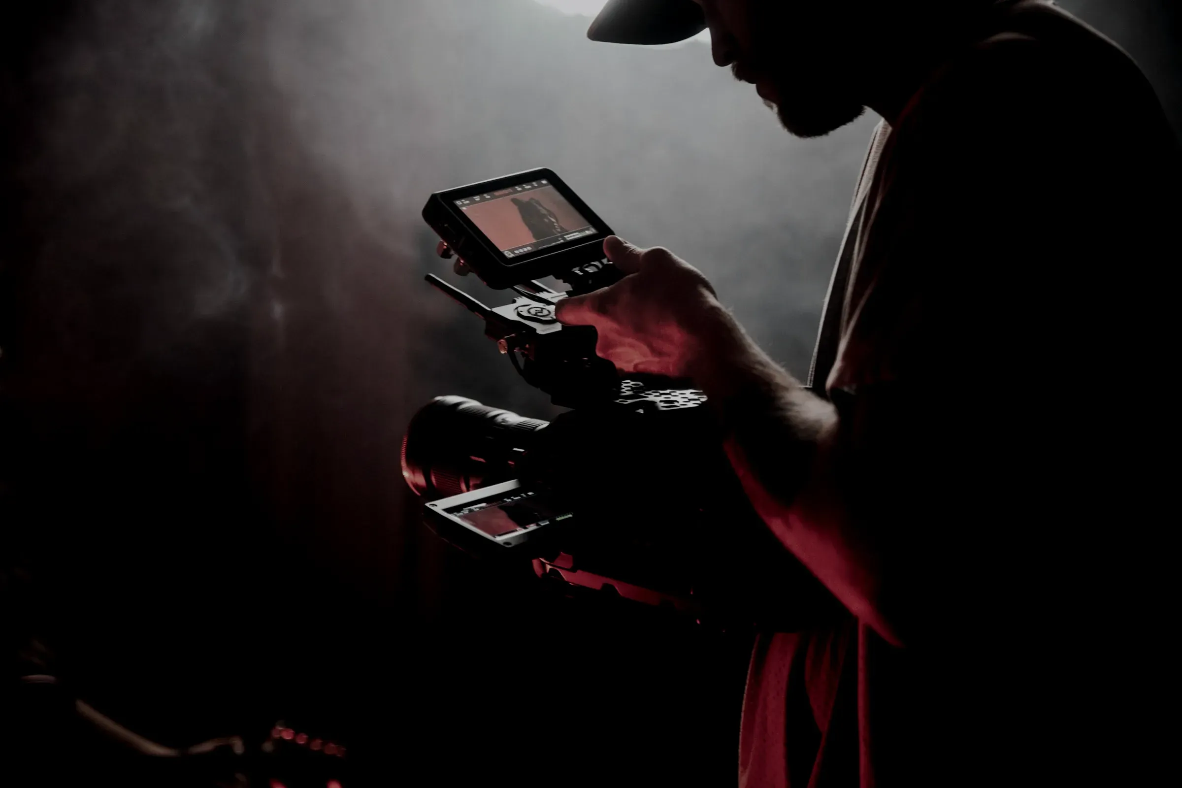 Filmfotograf med kamera och extern monitor i mörkt, rökfyllt motljus